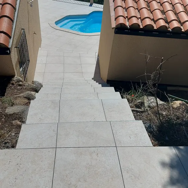 Terrasse et escalier extérieur carrelés en grès clair descendant vers une piscine