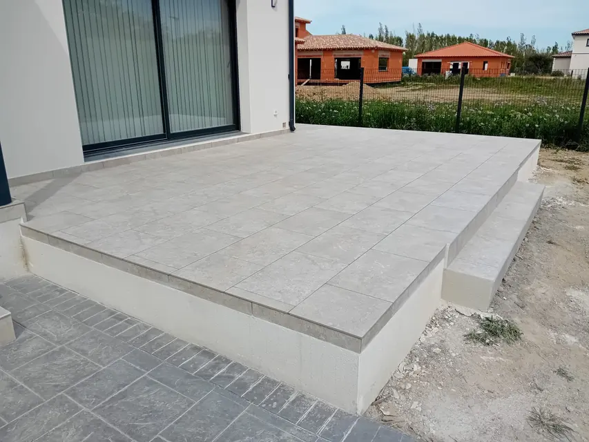 Terrasse surélevée carrelée avec ses marches, devant une baie vitrée