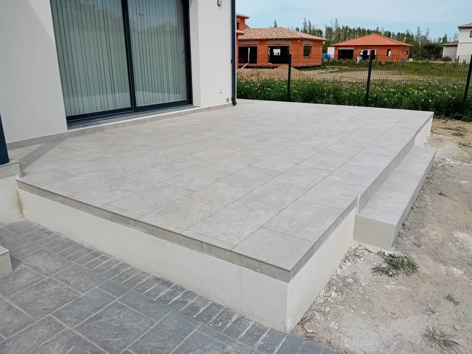 Terrasse surélevée carrelée avec ses marches, devant une baie vitrée
